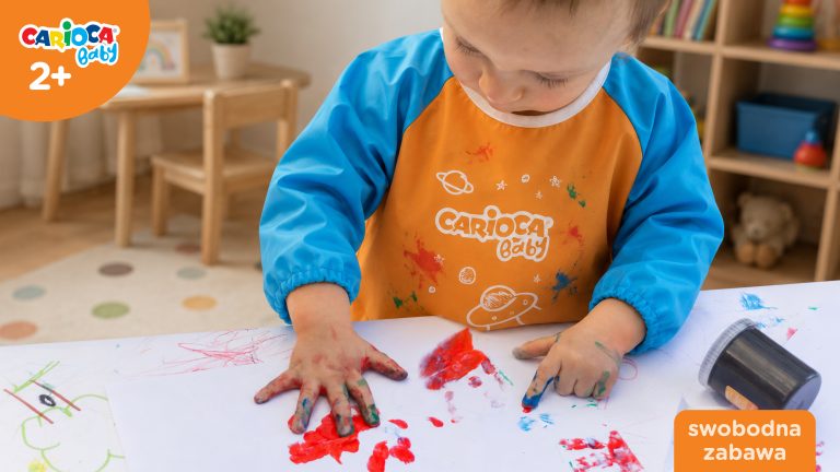 Dwulatek malujący farbami z ubrankiem zabezpieczonym przez fartuszek Carioca Baby podczas swobodnej zabawy plastycznej