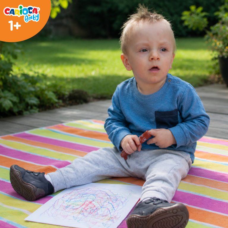 Roczne dziecko rysujące pisakami Misiakami Carioca Baby siedzące na kocyku w ogrodzie.